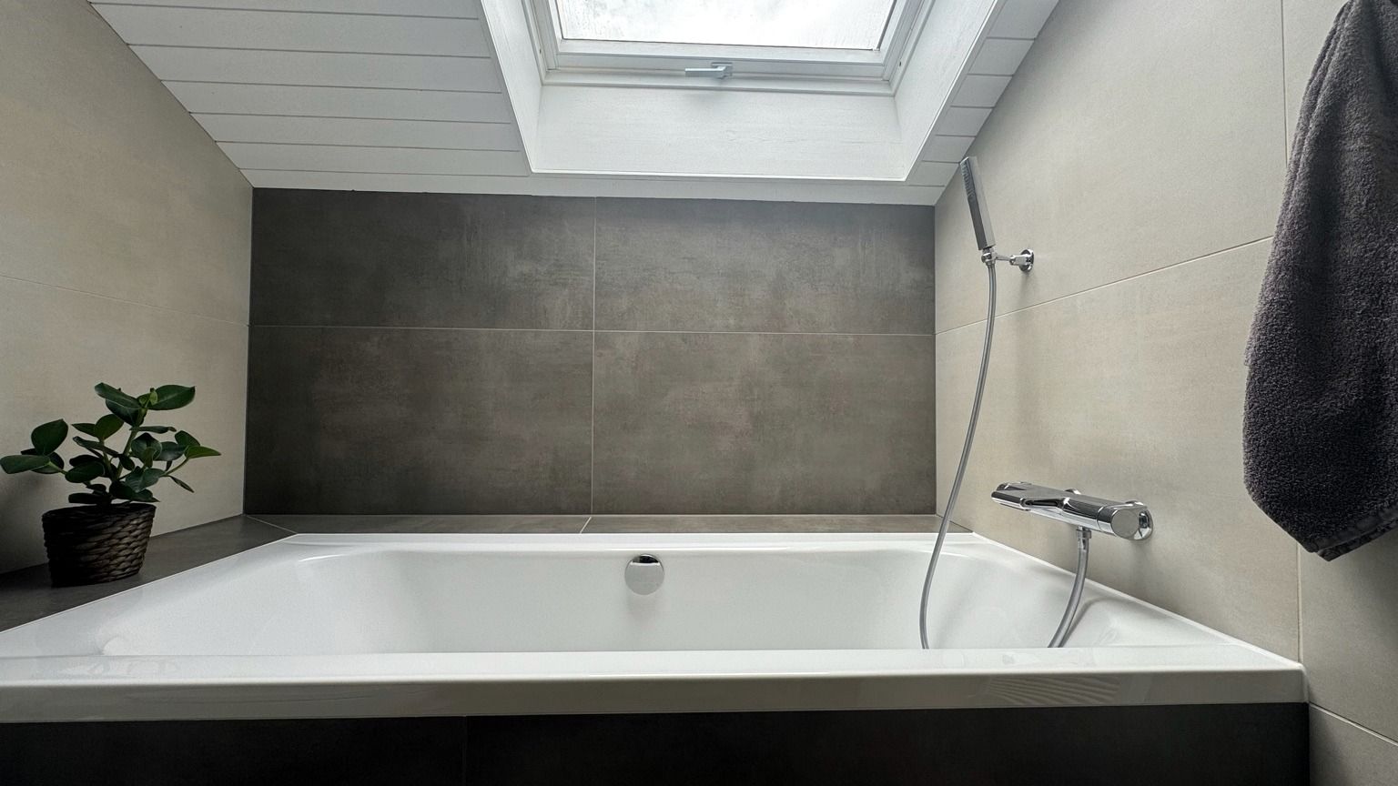 Baignoire encastrée sous la fenêtre de toit, murs en grands formats gris foncé et clairs