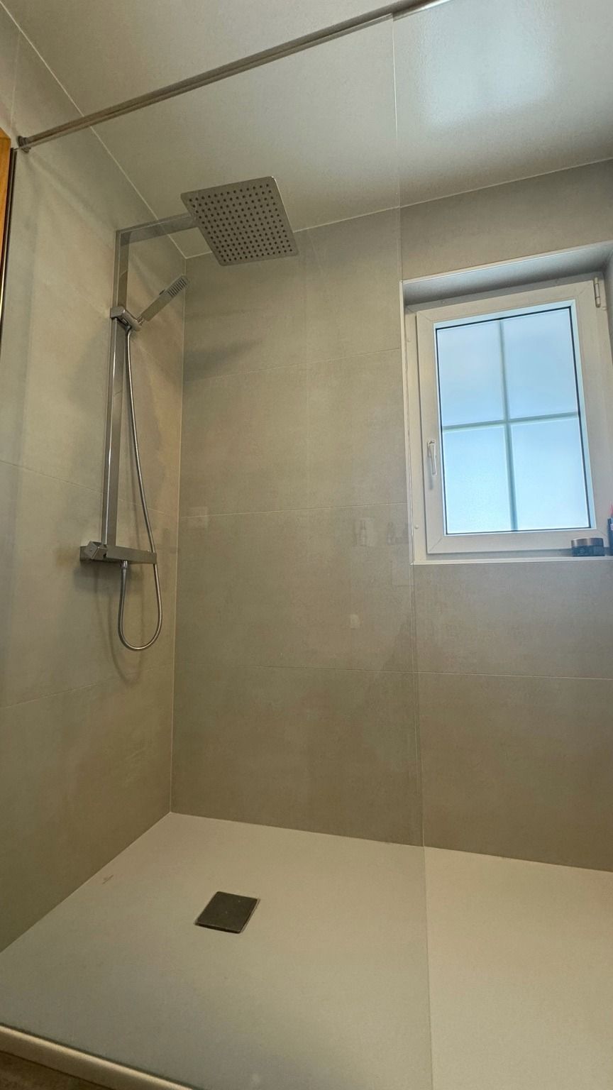 Douche de plain-pied avec murs en grands formats clairs, colonne de douche et petite fenêtre